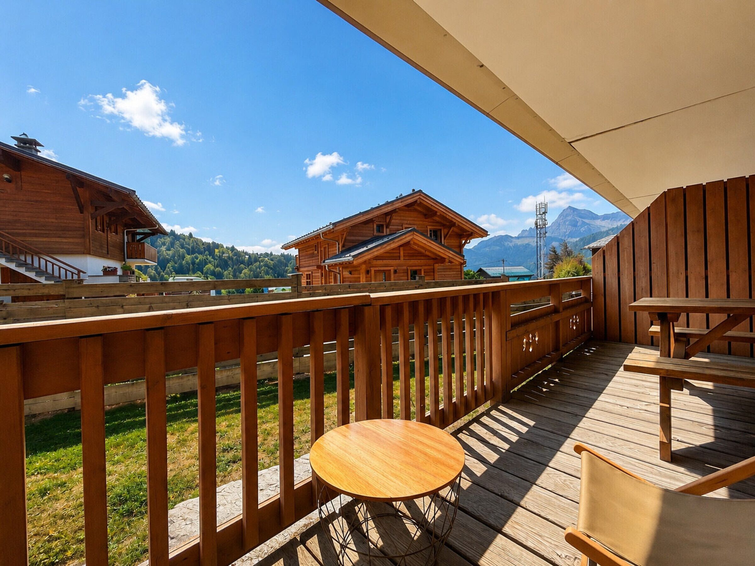 A wooden deck with a table and chairs, overlooking a mountain landscape and a wooden building.