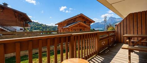 A wooden deck with a table and chairs, overlooking a mountain landscape and a wooden building.