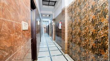 A corridor with marble walls, a tiled floor, and a fire extinguisher mounted on the wall.