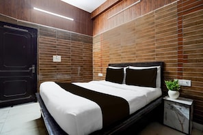 Une chambre d’hôtel moderne avec un grand lit, une table de chevet, une plante en pot et des panneaux de bois aux murs.