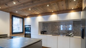 A modern kitchen with a wooden ceiling, built-in appliances, and a large window. - Chalet with pets - 14 guests (Les Gets)