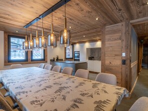 Ein modernes Interieur mit einem langen Esstisch, mehreren Stühlen und hängenden Pendelleuchten.