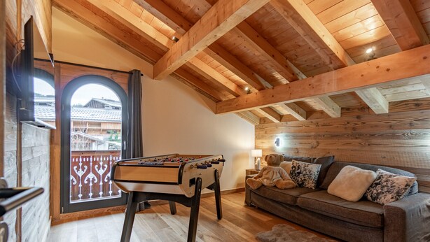 A cozy room with a wooden ceiling, a sofa, a table with a foosball table, and a view through a glass door. - Chalet with pets - 14 guests (Les Gets)