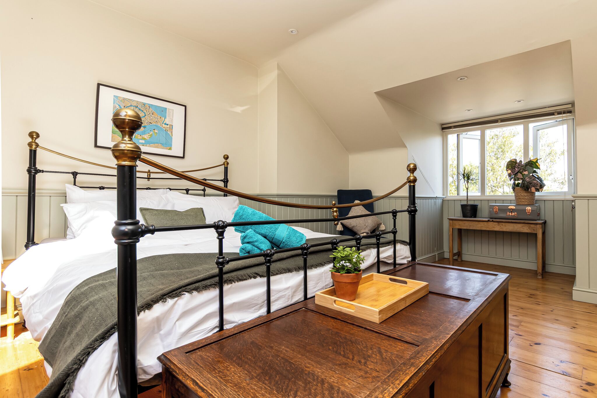A bedroom with a four-poster bed, a wooden nightstand, a potted plant, and a window with a view of trees.