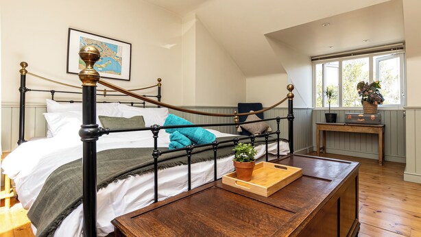 Una camera da letto con un letto a baldacchino, un comodino in legno, una pianta in vaso e una finestra con vista sugli alberi.