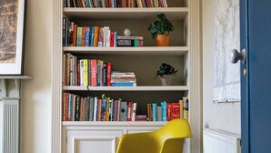 Una stanza con una libreria piena di libri, una sedia gialla e una pianta in vaso.
