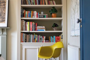 Ein Zimmer mit Bücherregal, einem gelben Sessel und einem Blumentopf.