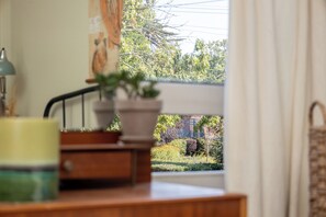 Vista dalla finestra su un giardino con una recinzione, una pianta in vaso su un tavolo e una lampada.