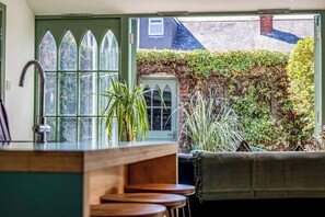 A kitchen with a green door, a window with a view of a brick wall and a house, and a plant on the counter. - Design-Led Edwardian Park-side Home Portsmouth - Holiday Home (Portsmouth)