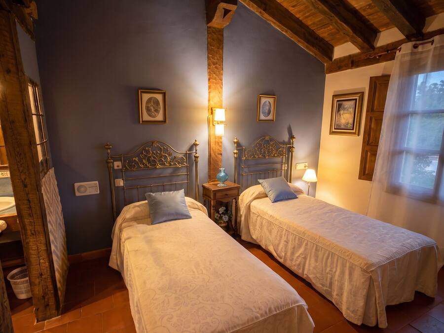 A room with two beds, wooden beams, a stone wall, and a window with a view.