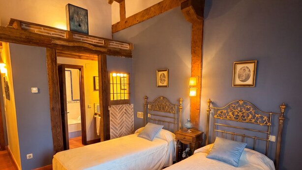 Ein Zimmer mit zwei Betten, Holzbalken an der Decke, einer Tür und einer Wand mit gerahmten Bildern.