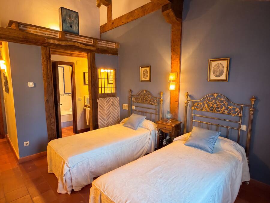 A room with two beds, wooden beams on the ceiling, a door, and a wall with framed pictures.