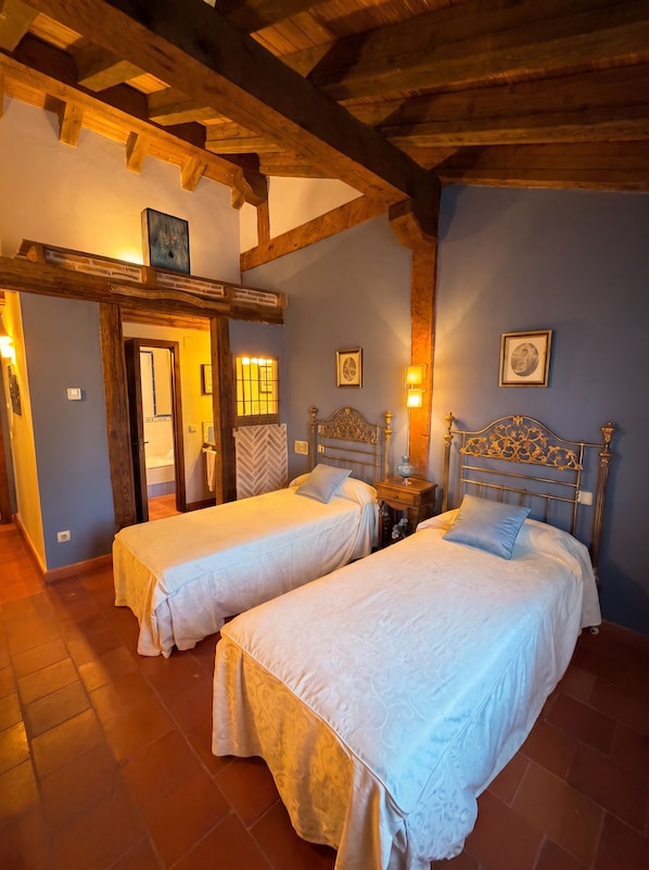 Una habitación con dos camas, vigas de madera en el techo, una puerta y una pared con cuadros.