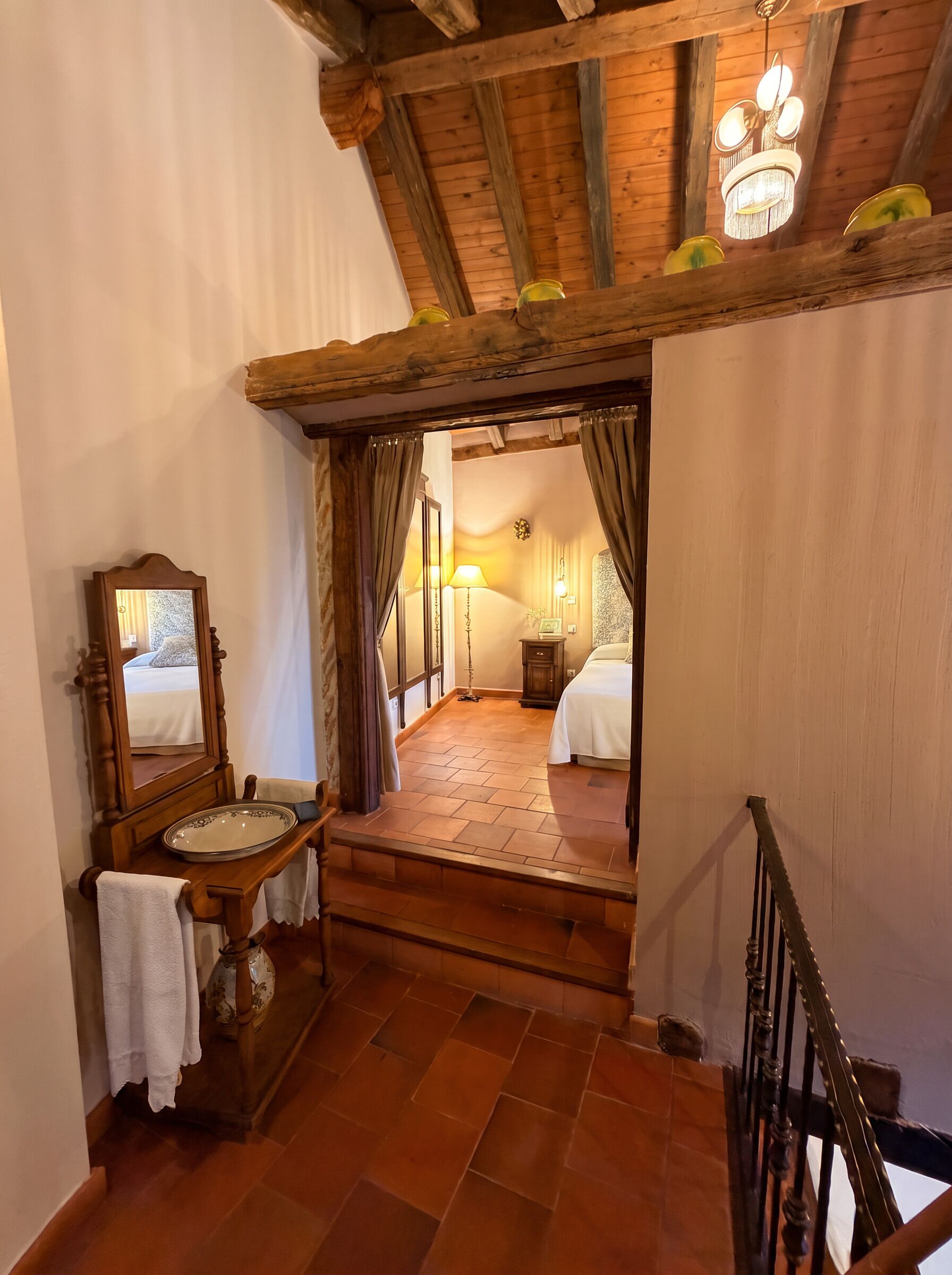 Een slaapkamer met een houten trap naar een bed, een nachtkastje met een lamp en een spiegel.