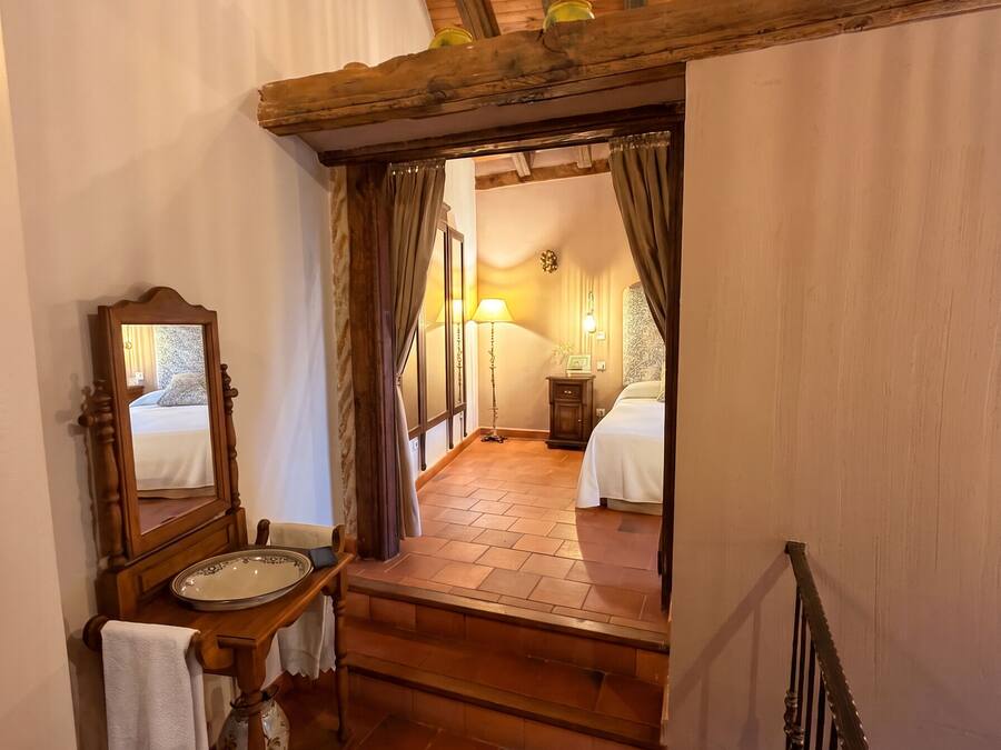 Una camera da letto con una scala in legno che conduce a un letto, un comodino con una lampada e uno specchio.