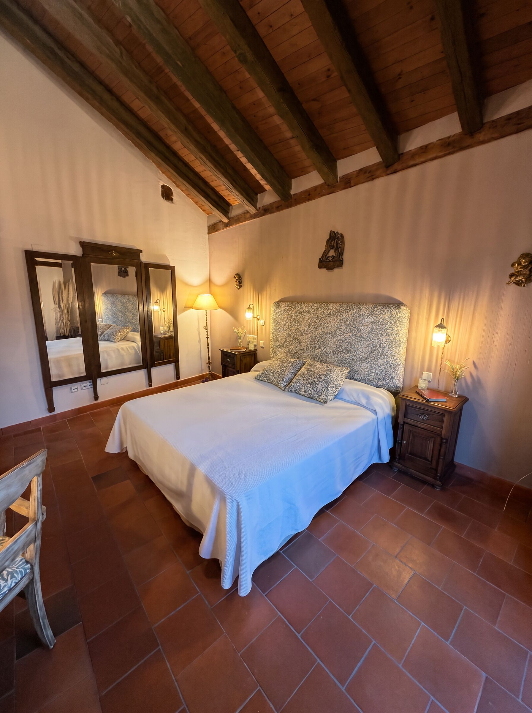 A bedroom with a large bed, a wooden ceiling, and a nightstand with a lamp.