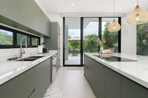 A modern kitchen with a large island, a built-in oven, and a view to an outdoor patio. - Casa Joanna | Luxury Jungle Retreat in Pacifico Resort | Private Pool (Pacifico Resort Lot 35)