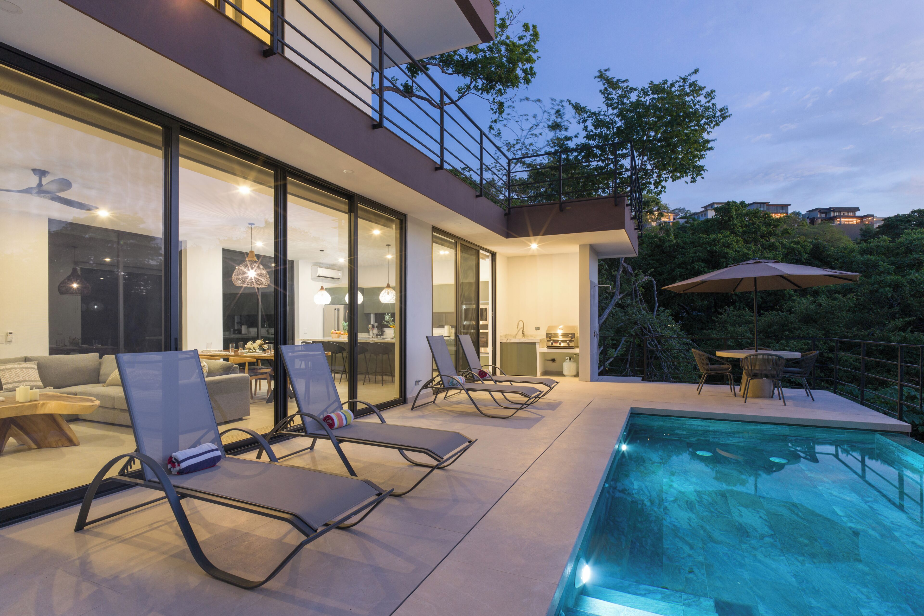 A modern house with a swimming pool, lounge chairs, and a dining area.