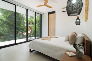 A modern bedroom with a large window, a bed with pillows, a hanging light fixture, and a potted plant. - Casa Joanna | Luxury Jungle Retreat in Pacifico Resort | Private Pool (Pacifico Resort Lot 35)