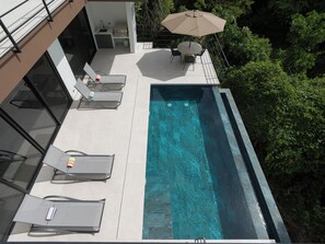A rooftop pool with lounge chairs and a table, surrounded by greenery. - Casa Joanna | Luxury Jungle Retreat in Pacifico Resort | Private Pool (Pacifico Resort Lot 35)