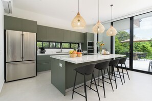 A modern kitchen with a large island, stainless steel appliances, and a view to the outdoors. - Casa Joanna | Luxury Jungle Retreat in Pacifico Resort | Private Pool (Pacifico Resort Lot 35)