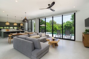 A modern living room with a grey sofa, dining area, and a view of a swimming pool. - Casa Joanna | Luxury Jungle Retreat in Pacifico Resort | Private Pool (Pacifico Resort Lot 35)