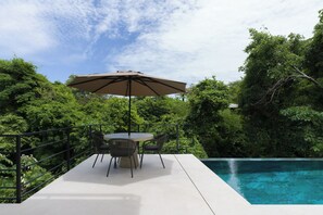 A patio with a table and chairs, an umbrella, and a pool. - Casa Joanna | Luxury Jungle Retreat in Pacifico Resort | Private Pool (Pacifico Resort Lot 35)