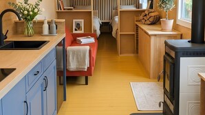 Una cocina moderna y compacta con estufa integrada, armarios de madera y un comedor con sofá rojo y mesa.