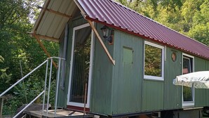 Una cabaña de madera verde con techo rojo, un porche y una zona de estar al aire libre cubierta.