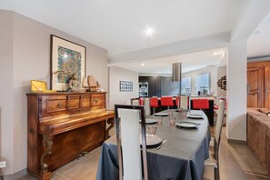 Un comedor con una larga mesa dispuesta para seis comensales, un piano de madera y una obra de arte enmarcada en la pared.
