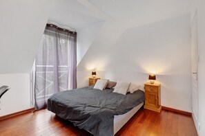 Une chambre à coucher avec un lit, deux tables de chevet avec des lampes, une fenêtre avec des rideaux et un plancher en bois.