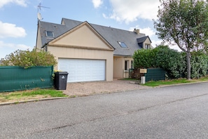 A residential house with a garage, a gravel driveway, and a green fence.