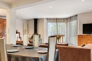 A dining area with a table set for four, a sofa, a television, and a window with curtains.