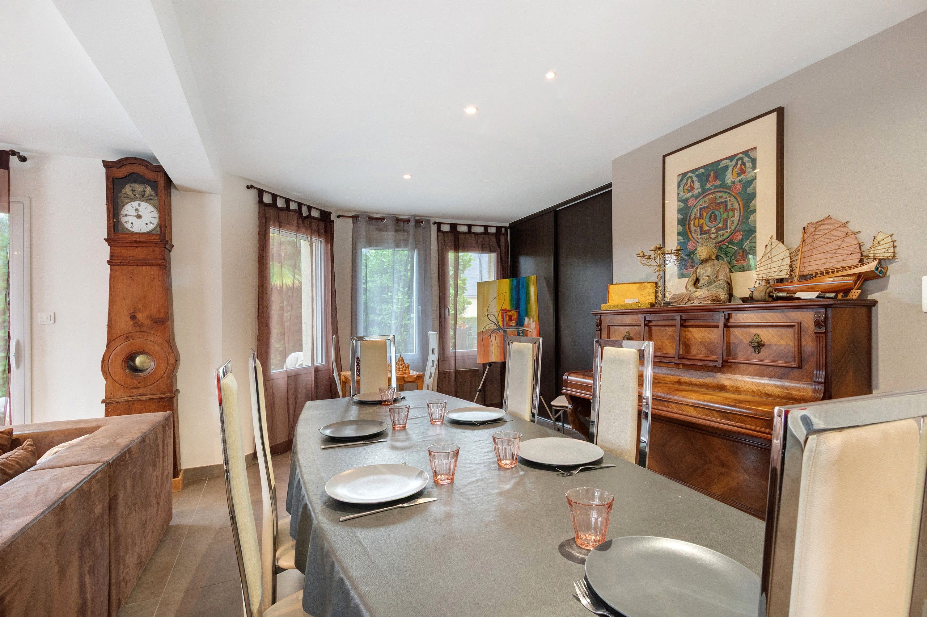 Une salle à manger avec une longue table dressée pour quatre personnes, un buffet en bois orné d’objets décoratifs et un grand tableau accroché au mur.