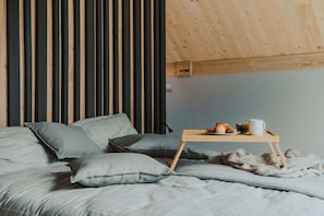Quarto com cama, almofadas, mesa de cabeceira com uma xícara e uma tigela de frutas.
