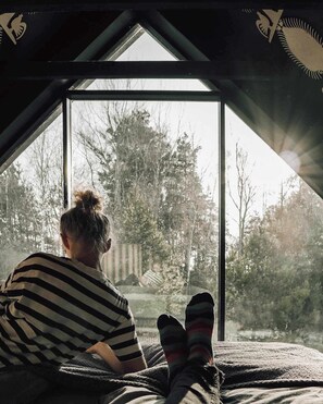 Una persona seduta su un letto in una stanza con una grande finestra, che guarda gli alberi.