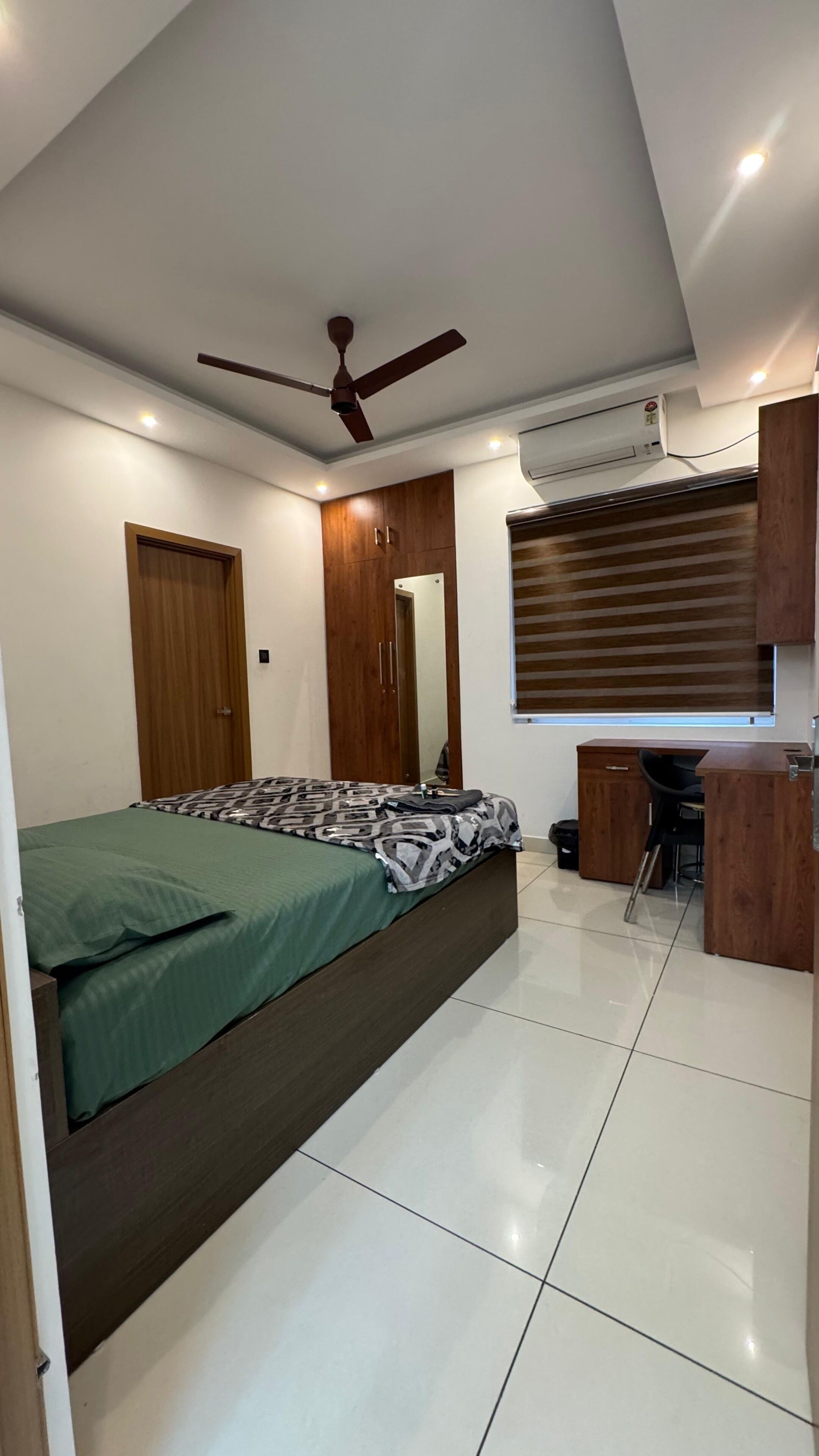 Ein Schlafzimmer mit einem Bett, einem Schreibtisch, einem Stuhl, einem Deckenventilator und einer Klimaanlage.