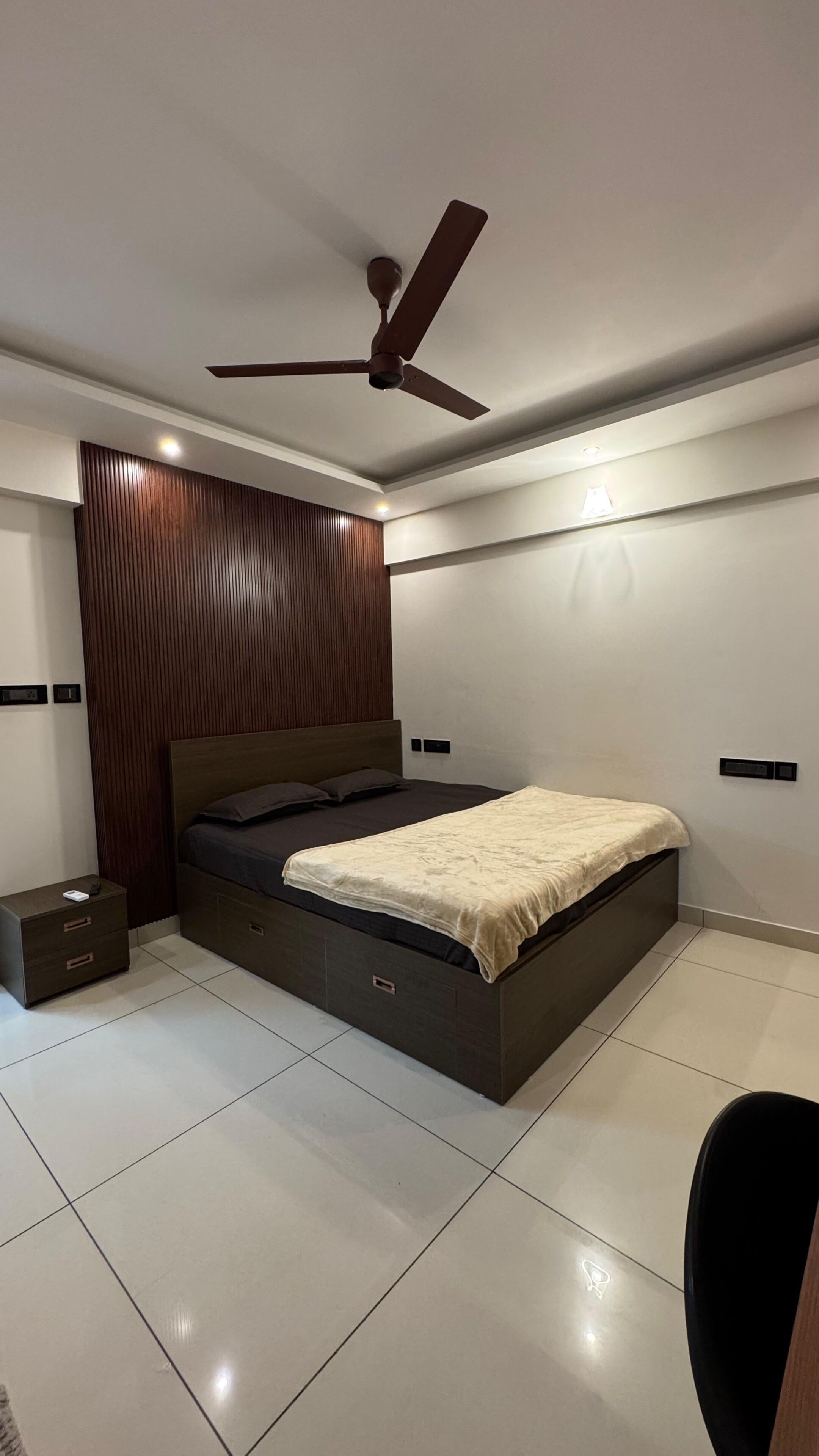 Une chambre à coucher moderne, équipée d’un lit, d’une table de chevet, d’un ventilateur de plafond et d’une lampe fixée au mur.