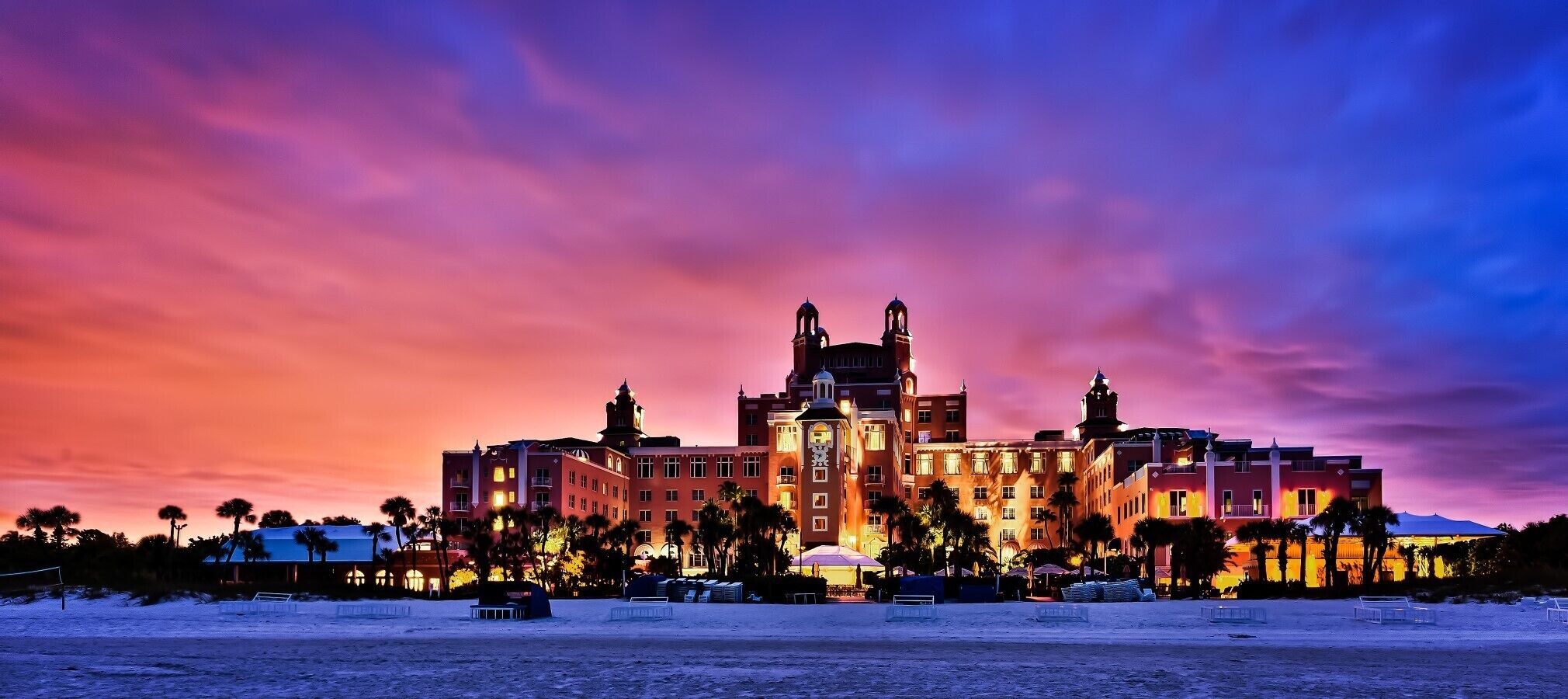 A hotel with a central clock tower, multiple balconies, and a beach in the foreground.