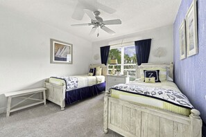 Ein Schlafzimmer mit zwei Betten, einem Deckenventilator, einem Fenster mit Vorhängen und einem kleinen Tisch.