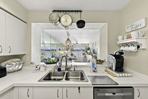 A modern kitchen with a large window, stainless steel appliances, and a coffee machine. - Serene Oasis | 2BR Club Bahia Condo | Isla Del Sol (Isla Del Sol)