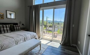 Een slaapkamer met een bed, een bankje, een nachtkastje en uitzicht door een schuifdeur op een terras.