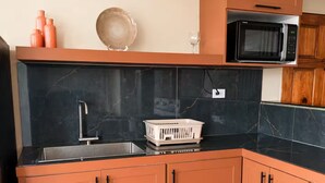 A compact kitchen with a black countertop, a sink, and a microwave. - Paramin View- 2 BR Ocean and Mountain Views Retreat (Diego Martin Regional Corporation)