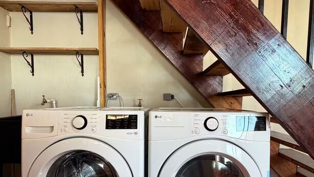Two front-loading LG washing machines in a room with a wooden staircase and a tiled floor. - Paramin View- 2 BR Ocean and Mountain Views Retreat (Diego Martin Regional Corporation)