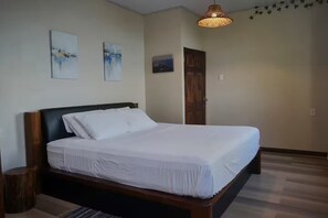 A neatly made bed with white linens in a room with a wooden headboard, a small wooden nightstand, and a woven light fixture. - Paramin View- 2 BR Ocean and Mountain Views Retreat (Diego Martin Regional Corporation)