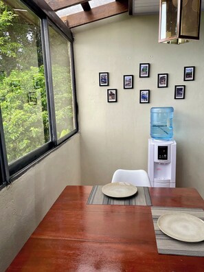 A dining area with a table, chairs, a water dispenser, and framed pictures on the wall. - Paramin View- 2 BR Ocean and Mountain Views Retreat (Diego Martin Regional Corporation)