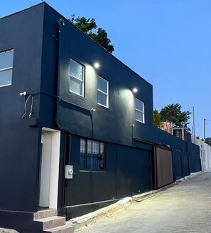 A modern two-story building with a dark facade, multiple windows, and a visible garage door. - Paramin View- 2 BR Ocean and Mountain Views Retreat (Diego Martin Regional Corporation)