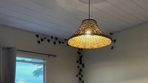 A room with a large window, a hanging woven light fixture, and a wall-mounted speaker. - Paramin View- 2 BR Ocean and Mountain Views Retreat (Diego Martin Regional Corporation)