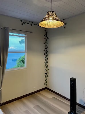 Ein Zimmer mit großem Fenster, einer hängenden gewebten Leuchte und einem Wandlautsprecher.