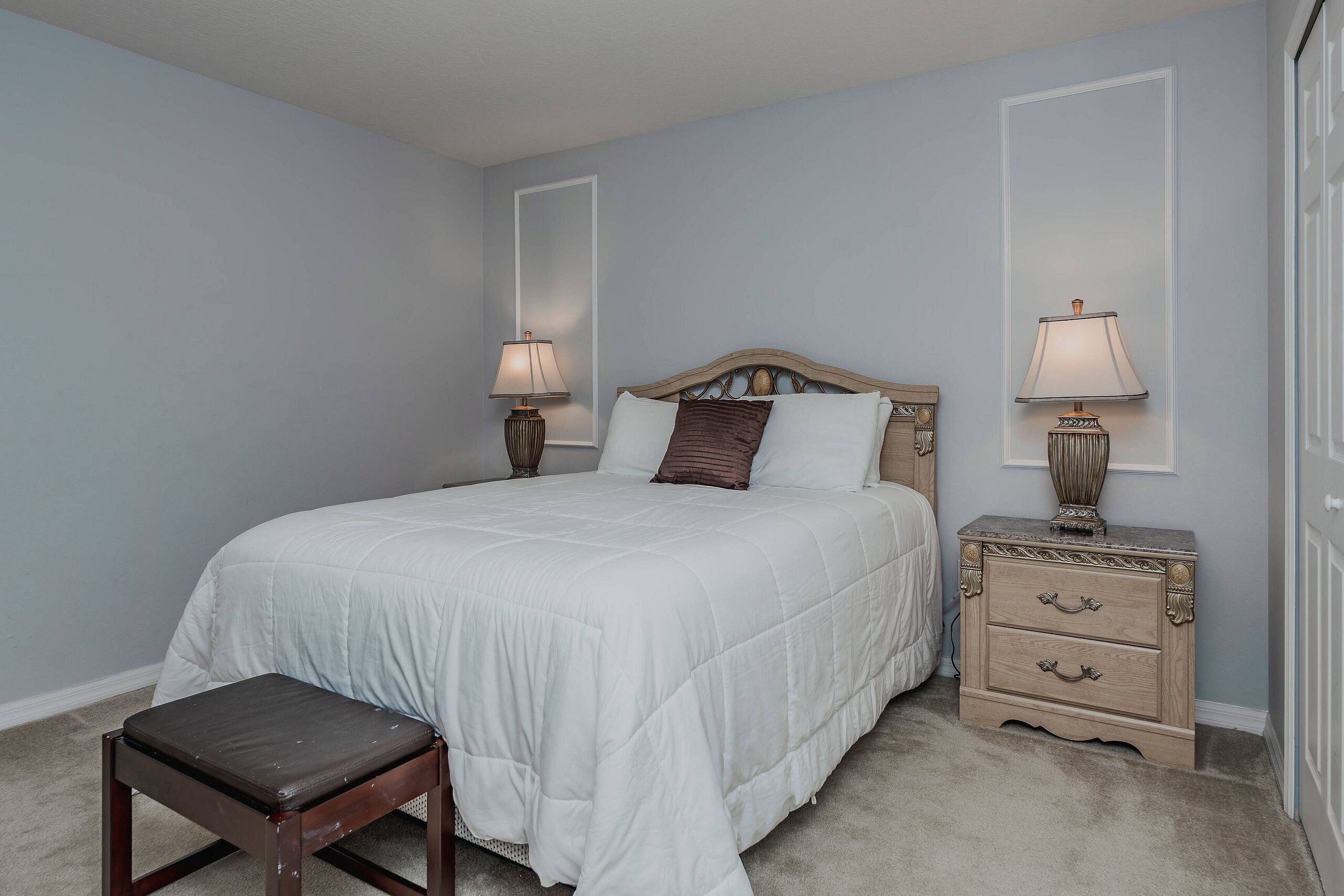 A bedroom with a single bed, bedside tables, a nightstand, and a bench.